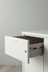 A partially open white drawer in a contemporary cabinet reveals light wood interior