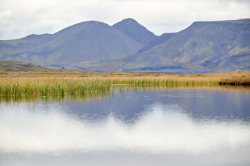 Calm lake reflecting mountains and cloudy sky in iceland