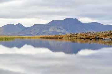 Mountains reflecting in calm lake under cloudy sky in iceland