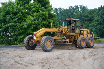 Fototapeta premium Motor grader smoothing surface for an even platform for new asphalt at highway construction site