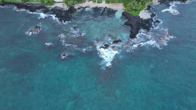 Overhead view waves break lava rock and sand beach