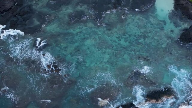 Overhead view waves break black lava rocks tide pool