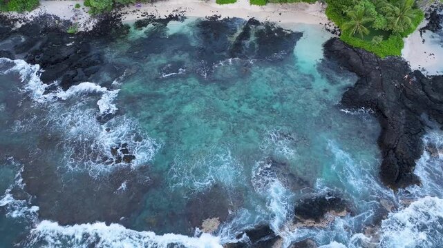 Overhead view waves break lava rock and sand beach