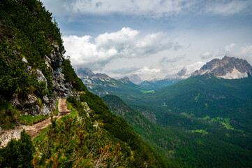 Breathtaking view of forests, mountains, and valleys in the Italian Dolomites (Dolomiti, Dolomiten). Captured from a scenic trail along a rocky ledge. Stunning alpine nature