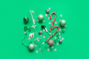 Glass with candy cane, Christmas balls and confetti on green background