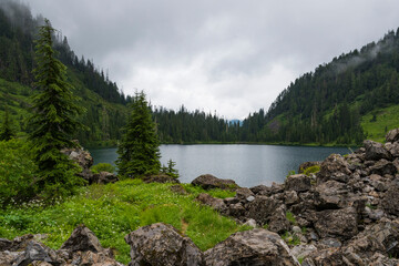 This picturesque view depicts a serene lake embraced by lush green mountains, creating a tranquil atmosphere that invokes feelings of peace and connection to nature.