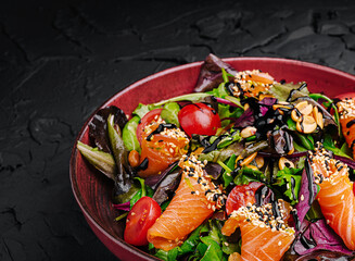 Colorful salad with salmon and fresh vegetables on a dark background