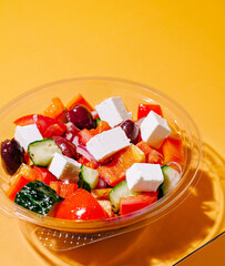 Fresh Greek salad with feta cheese and vegetables on orange background