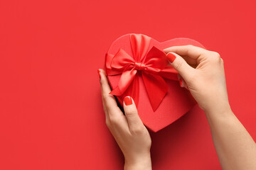 Female hands with red manicure and gift box on color background. Valentine's Day celebration