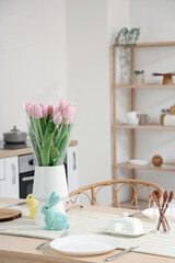 Vase with tulips and Easter rabbits on dining table in kitchen