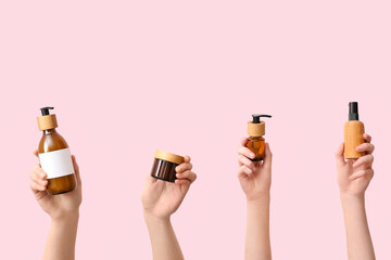 Women holding different cosmetic products on pink background