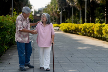 Senior husband helps support his wife who uses a cane to walking