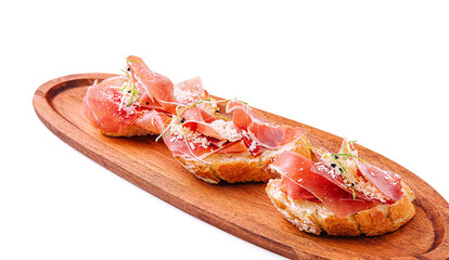 Delicious bruschetta topped with prosciutto and herbs on wooden board