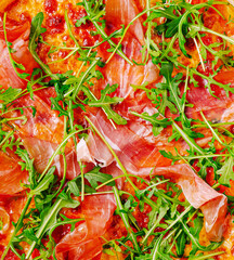 Freshly topped pizza with prosciutto and arugula on a wooden table
