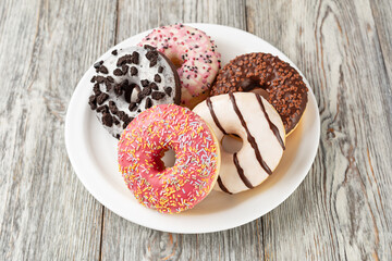 Delicious assorted donuts lying on white plate on wooden table
