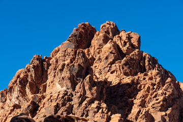 Fototapeta premium A striking rocky peak rises dramatically against a vibrant blue sky, conveying the raw beauty and power of nature’s stunning formations in a desert landscape.