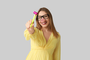 Beautiful young happy woman in funny disguise with party whistle on grey background. April Fools Day celebration