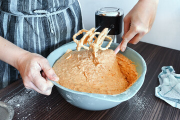 Woman cook wearing an apron on kitchen table mixes grated carrots in bowl to make carrot cake.