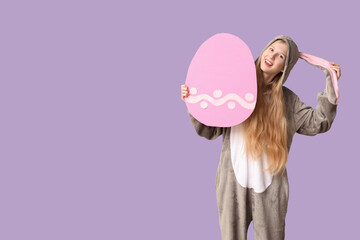Beautiful young happy woman in bunny costume with big paper egg on purple background. Easter celebration