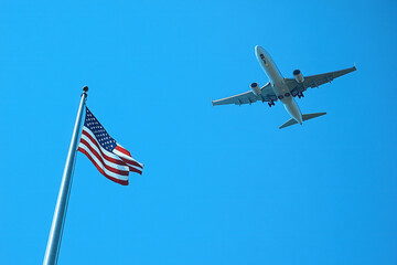 Bottom view of a passenger plane in the blue sky flying over the US flag. Travel concept in the USA.