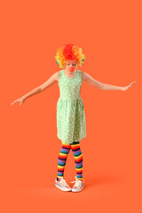 Funny girl in clown costume on orange background. April Fool's Day celebration