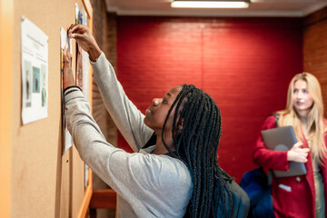 Young student putting up a notice on university bulletin board