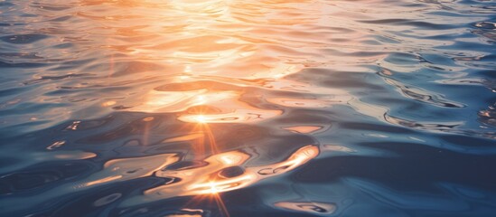 Glittering golden sunlight reflecting off serene blue water surface with gentle ripples creating a mesmerizing textured pattern in foreground.