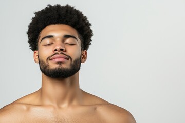 Fototapeta premium Young man with beard and curly hair meditating with closed eyes against neutral background. Calmness and mindfulness. Wellness and relaxation