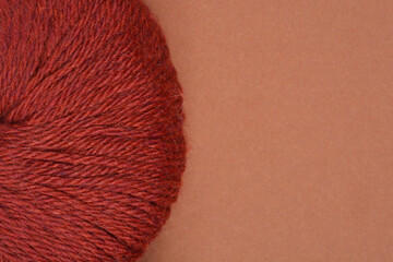 A close-up shot of deep red yarn against a solid brown background, highlighting its texture and color contrast