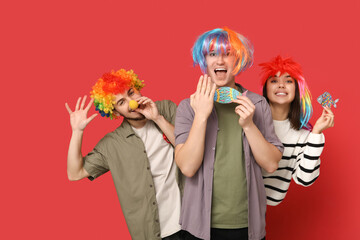 Young shocked friends in funny disguise with paper fishes on red background. April fool's day celebration