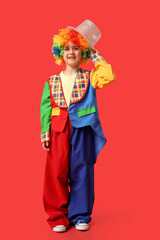 Funny little boy in clown costume with hat on red background. April Fools Day celebration