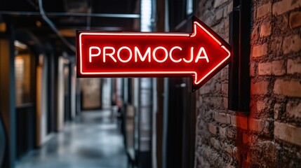 Neonowy znak "PROMOCJA" w kształcie strzałki w czerwonym kolorze, zamontowany w industrialnym korytarzu