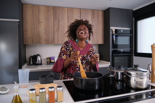 Happy African Woman Cooking Okra Soup with Spinach in Modern Kitchen