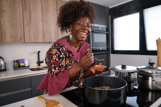 African woman tasting okro soup with spinach cooking in kitchen