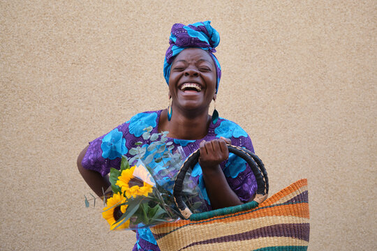 Happy African woman holding sunflowers and a colorful bag is laughing