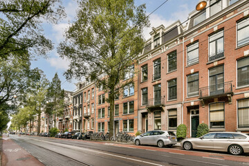 Fototapeta premium A scenic urban street lined with stylish residential buildings, lush trees, parked bicycles, and cars creating a vibrant city atmosphere.