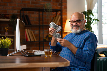 Indian elderly man counting five hundred rupee notes while sitting at his desk at home