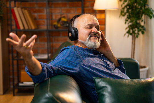 Senior man with beard wearing kurta, relaxing and enjoying music on headphones at home