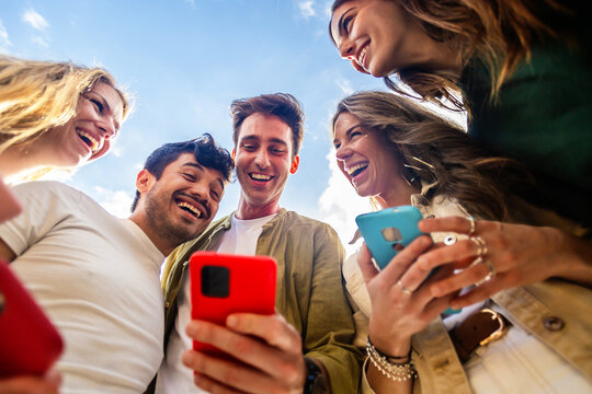 Group of young people using mobile phones, enjoying social media content against blue sky. Social media and technology lifestyle concept