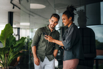 Multiracial colleagues discussing startup project and smiling during workday in office interior