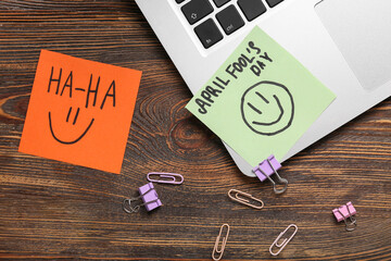 Laptop, paper clips and sticky notes on wooden background. April Fools Day prank