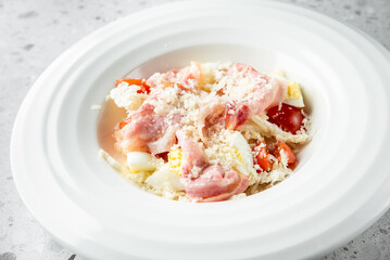 A close-up view of a dish featuring pieces of meat, chopped vegetables, and boiled eggs served in a white bowl, showcasing a fresh and appetizing meal.

