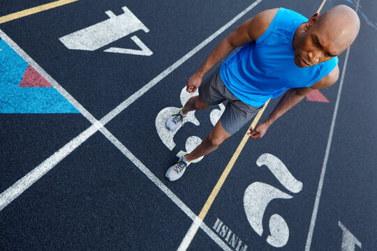 Black man, fitness and runner with track at stadium for race, sprint or sport marathon above. Top view, African athlete or male person with number for competition or running challenge on asphalt
