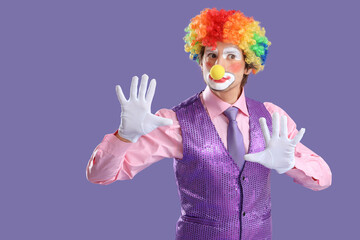 Portrait of pantomimist clown touching invisible wall on lilac background. April Fool's day...