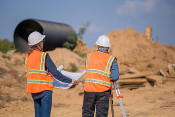 Construction surveyor or engineer working construction site blueprint and theodolite mounted tripod...