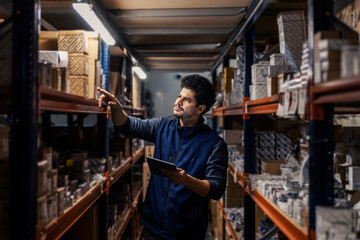 Interracial storage worker with tablet in hands inventorying shipments and goods in warehouse.