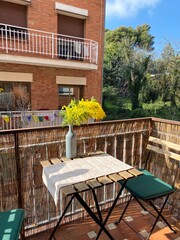 Sunny balcony with cozy bistro table and bright yellow flowers, ideal for spring mornings, urban living