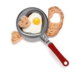 Frying pan with heart-shaped fried egg and bread on white background