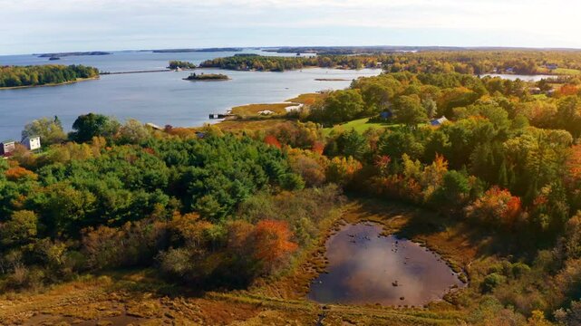 Aerial drone shot over the coastline of Oak Island, Nova Scotia, Canada.
High view of the sea, autumn colorful trees foliage. Picturesque landscape. Fall vibrant colors.