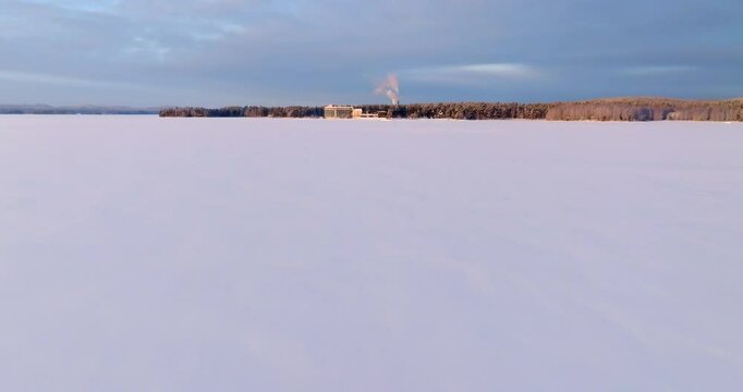 Aerial view low over snowy ice on lake Pielinen, sunny, winter evening in Finland